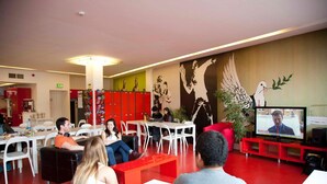 Un espace détente moderne, avec des meubles rouges et blancs, une grande fresque murale et un écran de télévision diffusant une vidéoconférence.