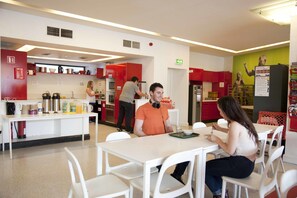 A cafeteria with white tables and chairs, a man in an orange shirt, and a woman in a white top. - Abigails Hostel (Dublin)