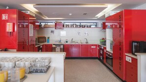 Une cuisine avec des placards rouges portant les inscriptions « RÉFRIGÉRATEUR DU PERSONNEL » et « CLIENTS ». On y trouve des appareils de cuisine, un évier et un plan de travail sur lequel sont disposés divers objets.
