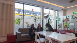 Une pièce avec un canapé, une table et des chaises. De grandes fenêtres offrent une vue sur un train et sur quelques espaces verts à l’extérieur.