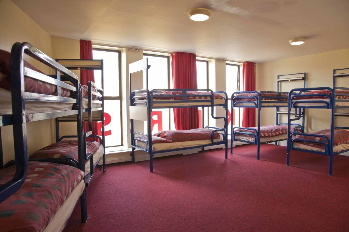 A dormitory room with bunk beds, red curtains, and a window with a view.