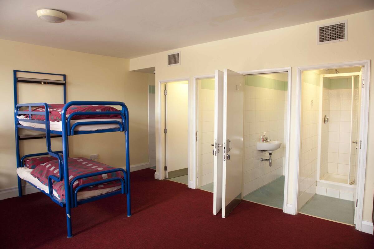 A room with bunk beds, a bathroom with a shower, and a sink.