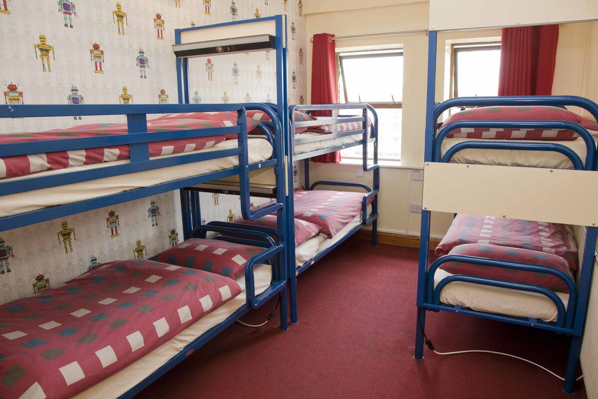 A dormitory room with bunk beds, a window with red curtains, and a wall with a robot pattern.