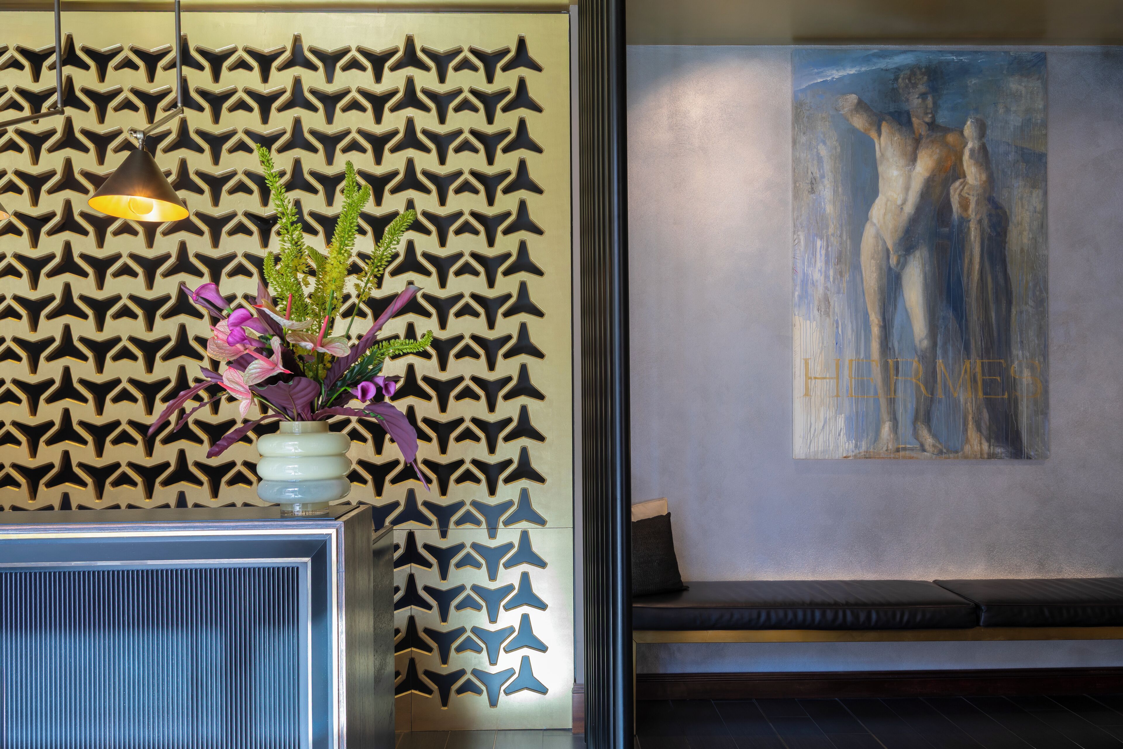 A reception area with a patterned wall, a vase with flowers, and a painting.