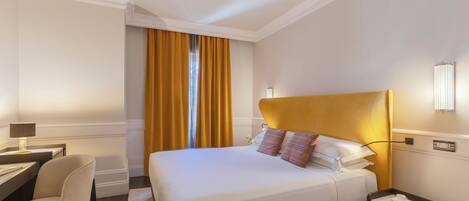 Une chambre d’hôtel comprenant un lit, une table de chevet, une lampe, une chaise et un bureau avec une lampe.