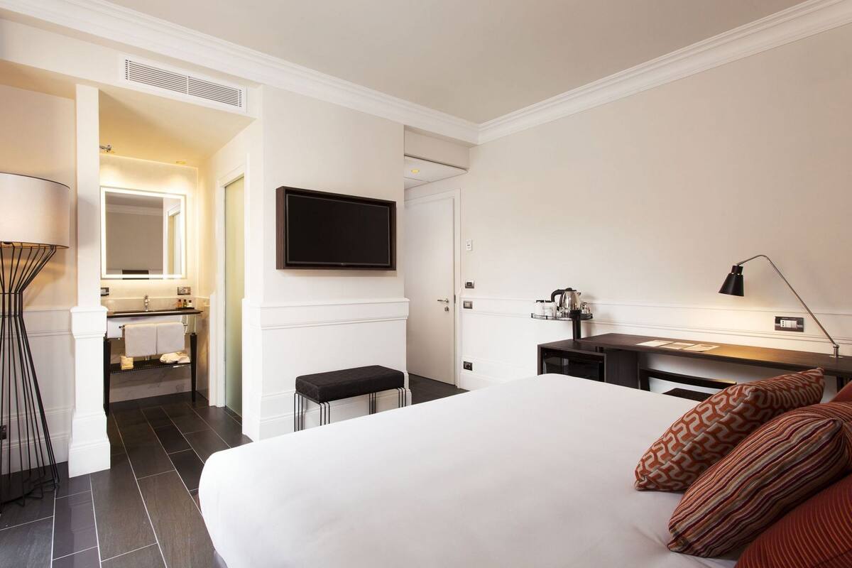 A hotel room with a bed, a desk, a TV, a mirror, and a bathroom.