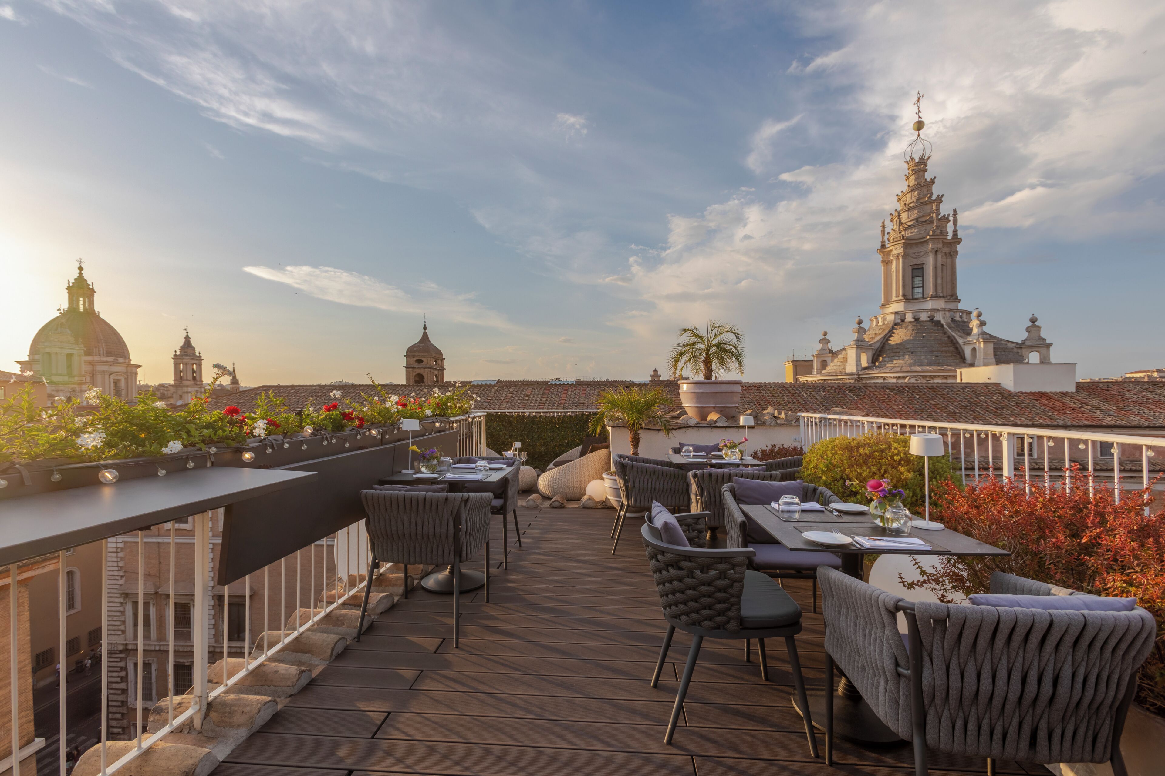 A rooftop terrace with outdoor seating, a view of historic buildings, and a clear sky.