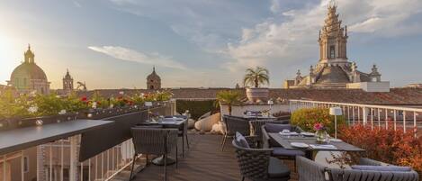 A rooftop terrace with outdoor seating, a view of historic buildings, and a clear sky.