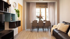 A modern living room with a dining area, a black leather sofa, a TV, and a bookshelf. - Easy Sleep Eixample  (Barcelona)