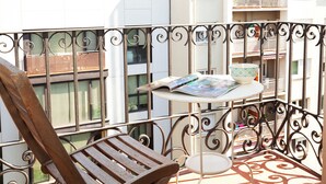 A balcony with a wooden chair, a small table with a magazine and a bowl, and a view of neighboring buildings. - Easy Sleep Eixample  (Barcelona)