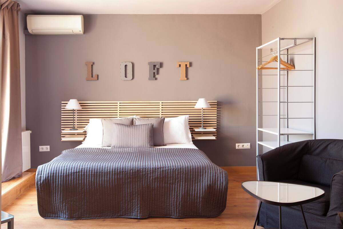 Quarto moderno com cama, luminárias de cabeceira, guarda-roupa e uma pequena mesa.
