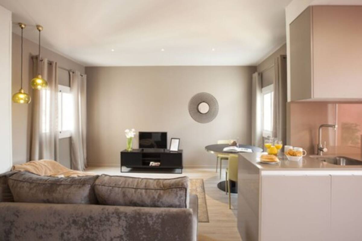 Uma sala de estar moderna com um sofá, uma TV sobre um suporte preto, e uma área de jantar com uma mesa e cadeiras.