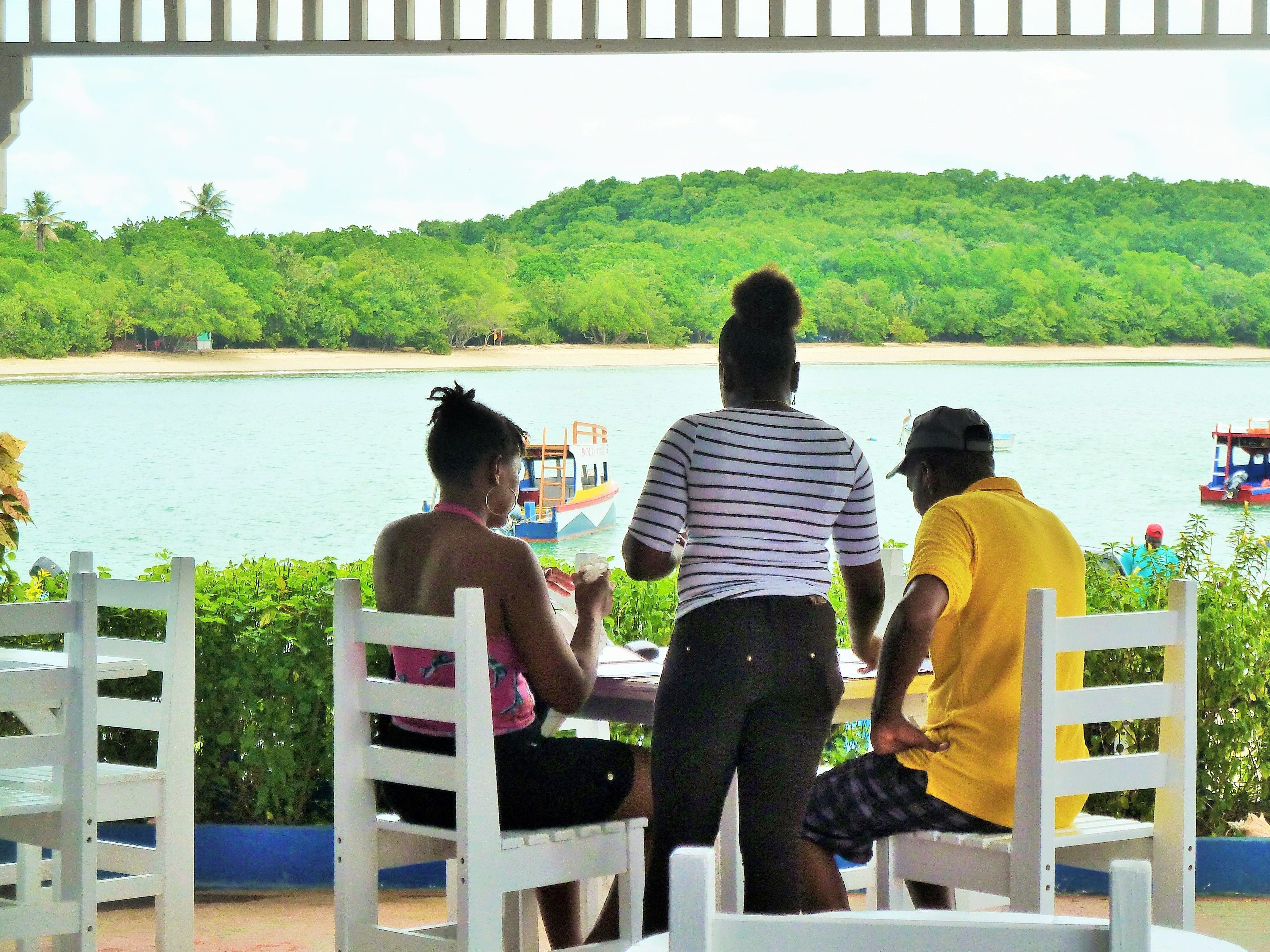 Three people seated at a table with a view of a beach and boats in the distance.