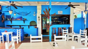 A bar area with white chairs and tables, blue walls, and ceiling fans. - Miller's Guest House (Buccoo)