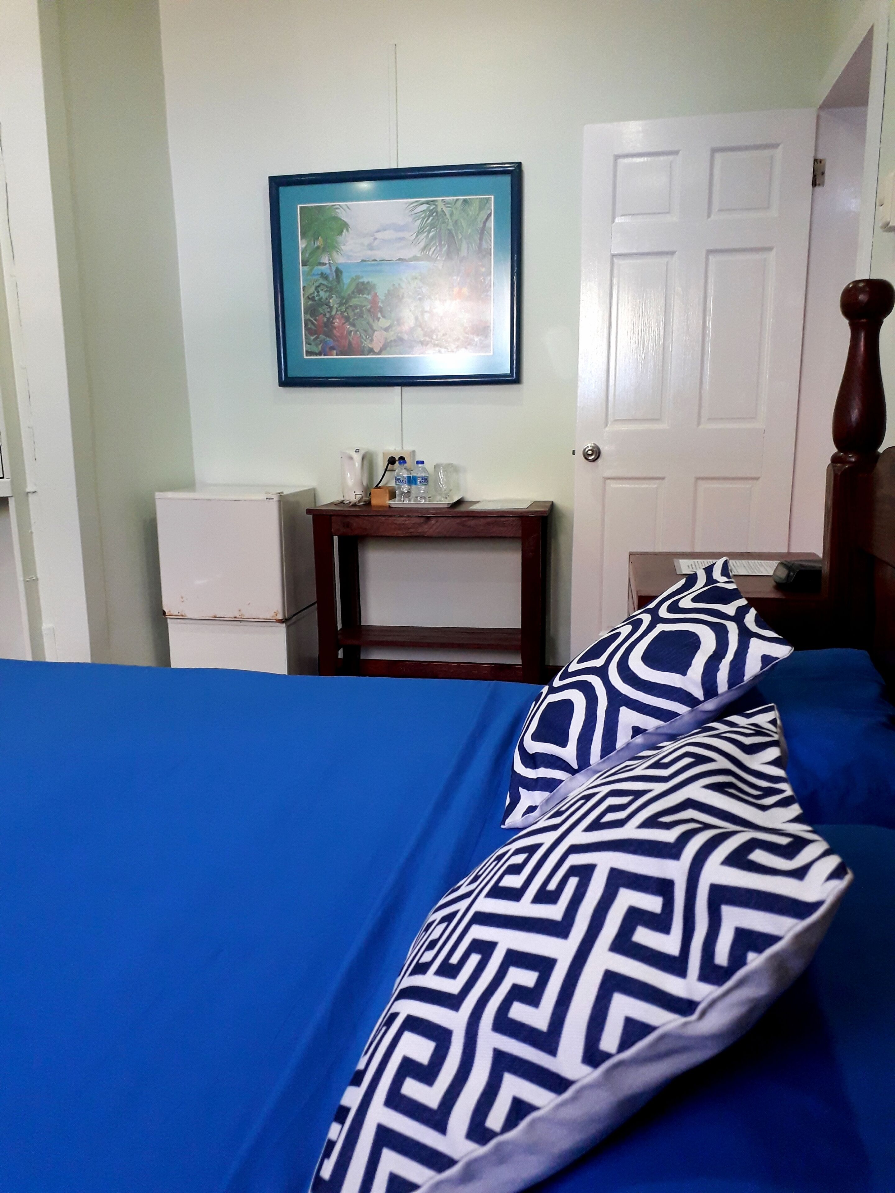 Un dormitorio con cama, mesita de noche, un cuadro enmarcado en la pared y una puerta.