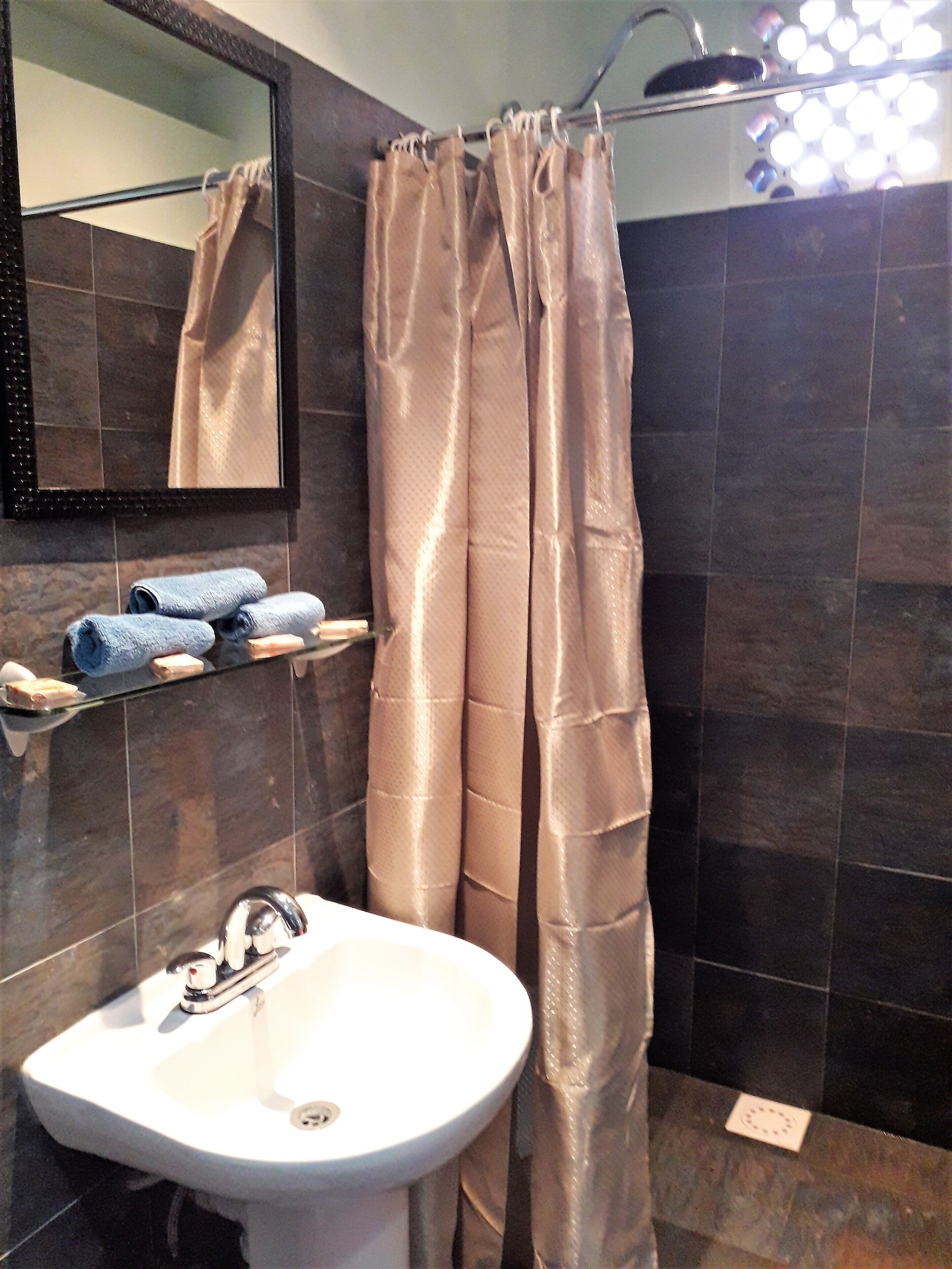 A bathroom with a white sink, dark tiled walls, a shower curtain, and a mirror.