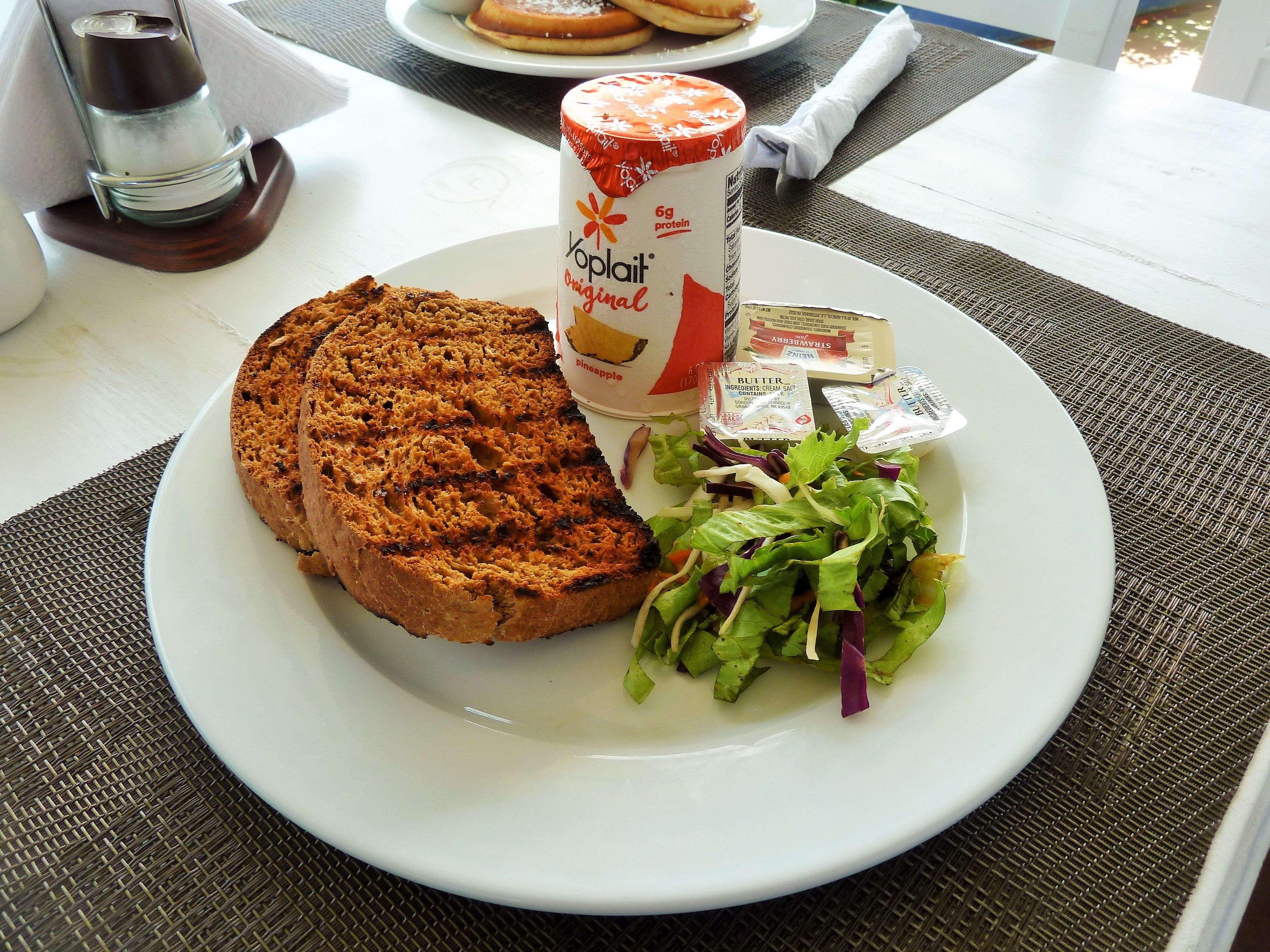 A plate with a slice of pineapple cake, a can of Yoplait Original, and a salad with butter packets.
