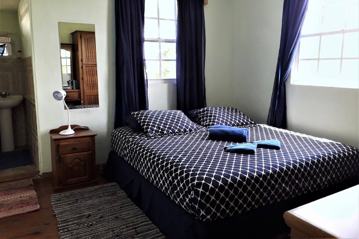 A bedroom with a bed, a bedside table, a mirror, a window with curtains, and a wooden cabinet.