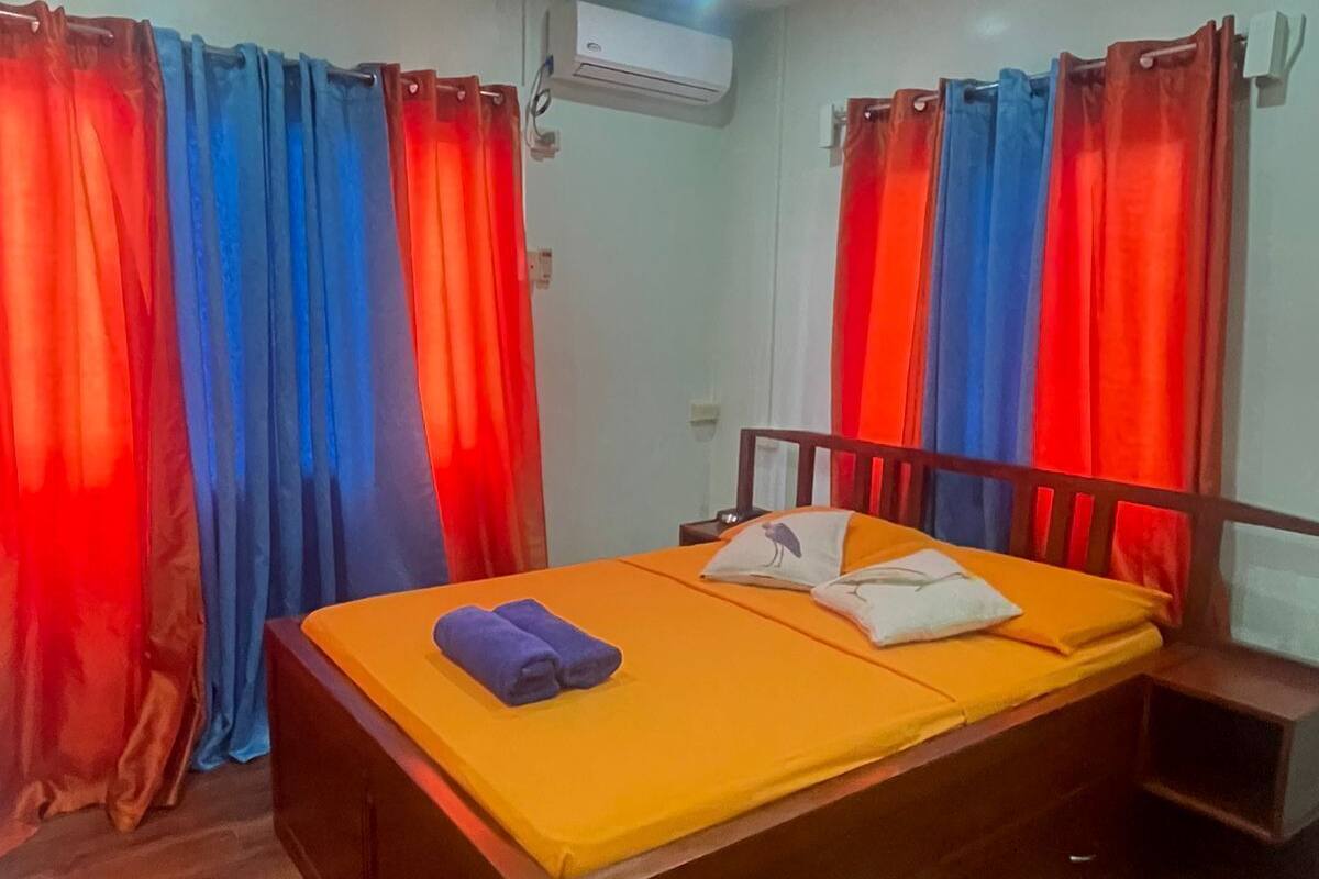 A room with a bed, curtains, an air conditioning unit, and a wooden floor.