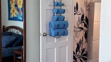 A room with a bed, a door with towels, a shower with a leaf pattern, and a painting on the wall.