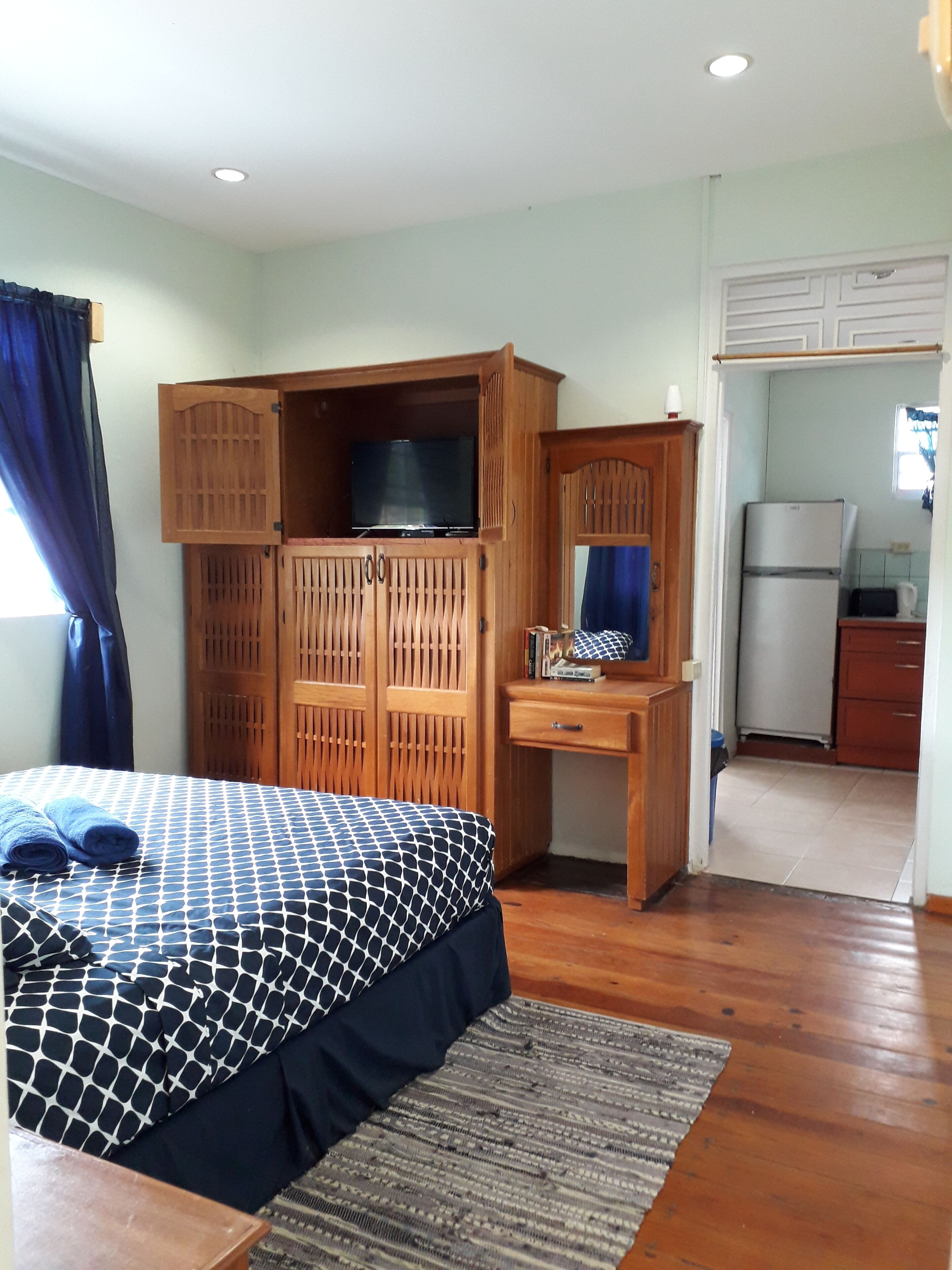 Ein Schlafzimmer mit einem Bett, einem Holzschrank, einem Schreibtisch und einer Küchenzeile.