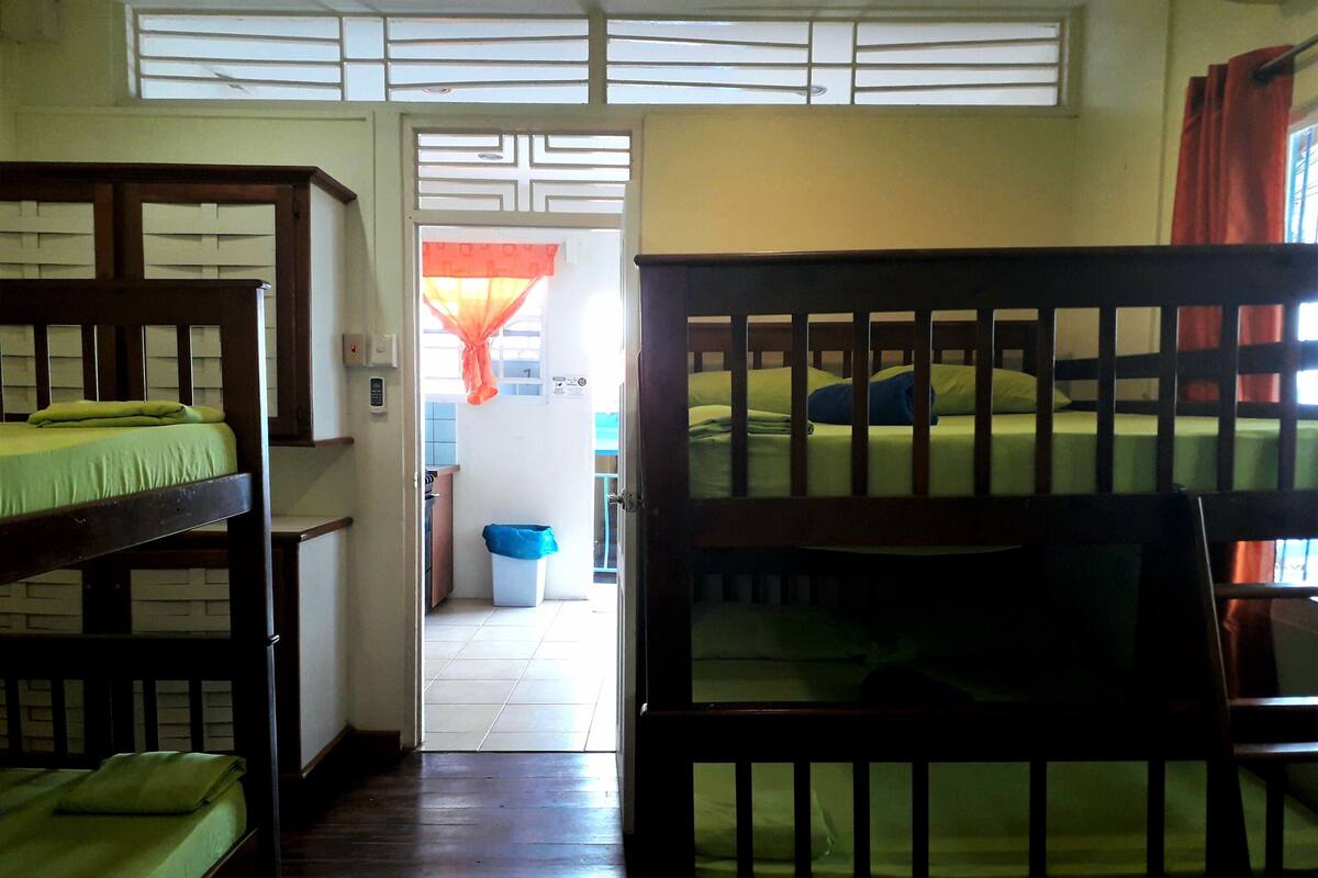 A dormitory room with bunk beds, a small kitchen area, and a bathroom visible through an open door.