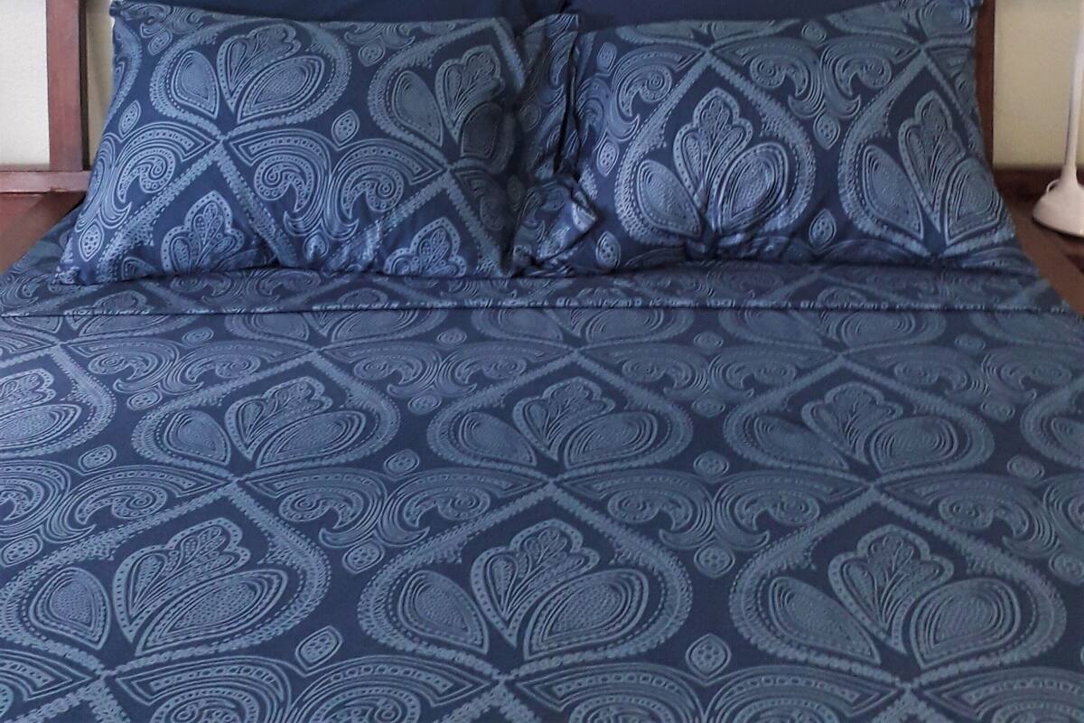 A bed with a blue patterned bedspread and matching pillows, a colorful tapestry with fish and a seahorse on the wall above, and a wooden headboard.
