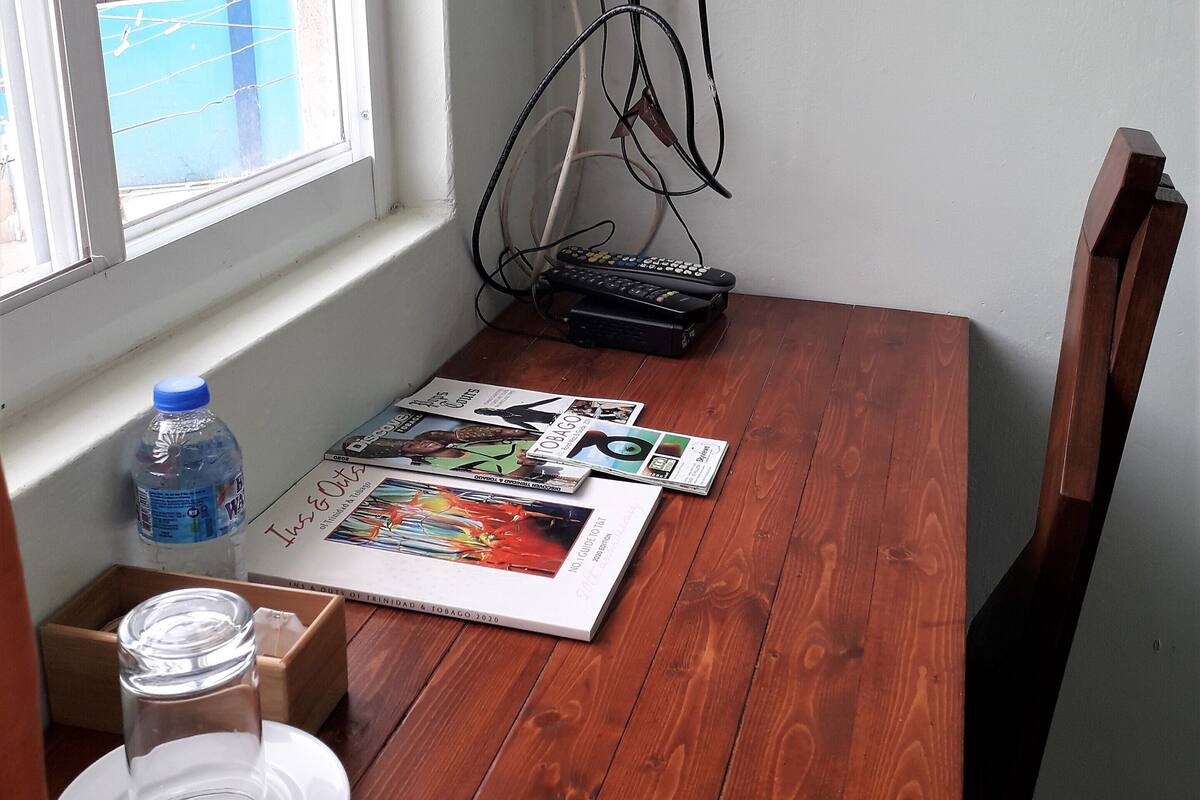 A wooden table with magazines, a water bottle, and a glass. A TV is mounted on the wall above the table.