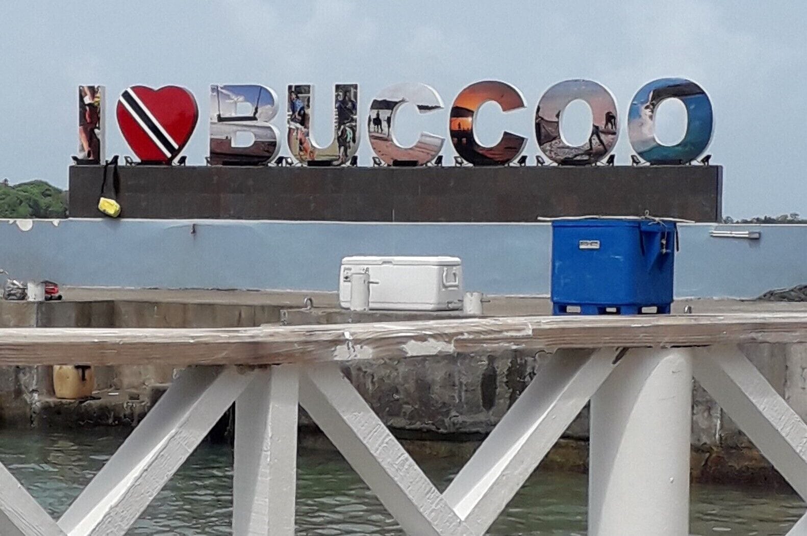 A dock with a sign that reads "I ❤️ BUCCOO" and a blue cooler on the dock.