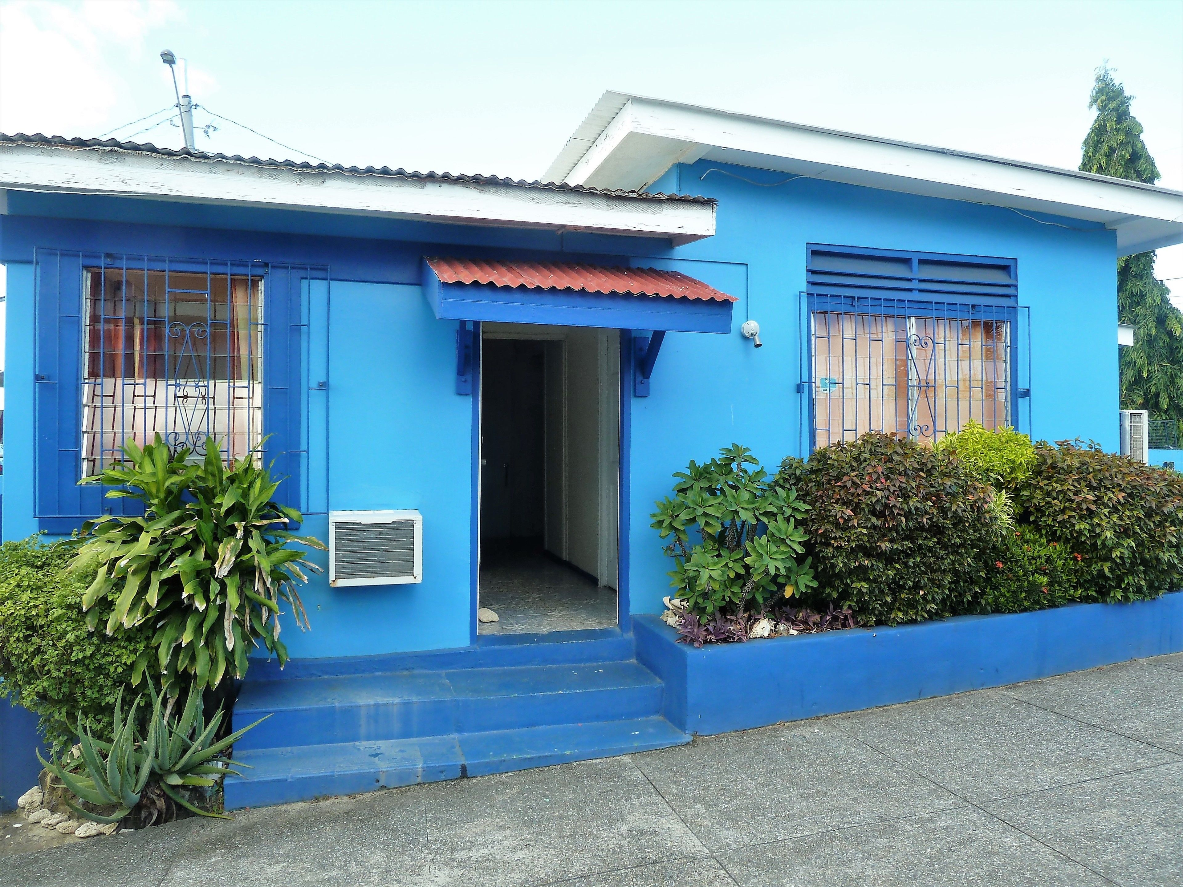 Una casa azul con techo de metal, un pequeño porche y una ventana con barrotes.