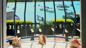 A balcony with a view of turquoise water and boats, surrounded by a railing and some greenery. - Miller's Guest House (Buccoo)
