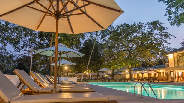 A poolside area with lounge chairs and umbrellas, a pool, and a building with outdoor seating. - The Lakeside Hotel at Nuwarawewa (Anuradhapura)