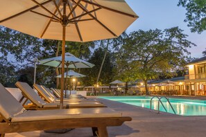 Un espace aménagé au bord de la piscine, avec des chaises longues et des parasols, une piscine, et un bâtiment doté d’une terrasse.