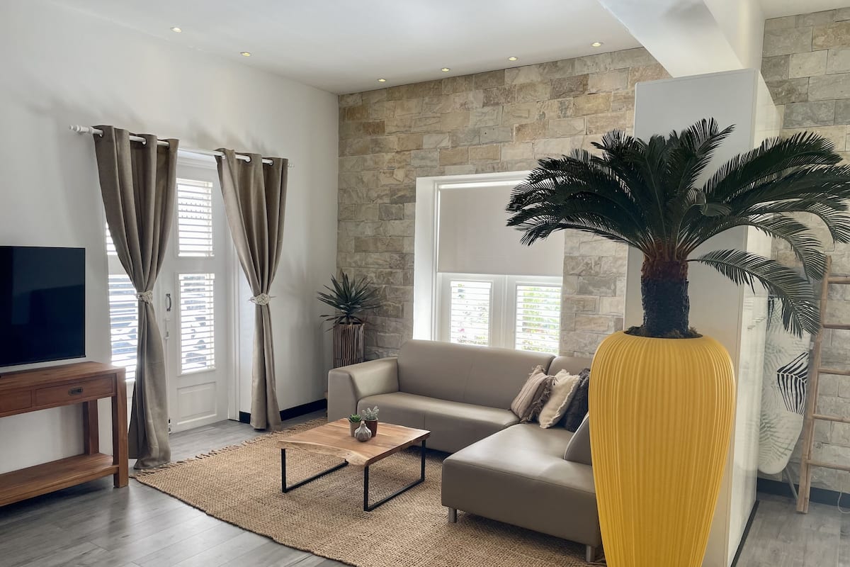 Un salon moderne avec un mur d’accent en pierre, un grand canapé, une table basse et un vase jaune.