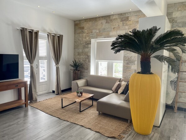 Un salon moderne avec un mur d’accent en pierre, un grand canapé, une table basse et un vase jaune.
