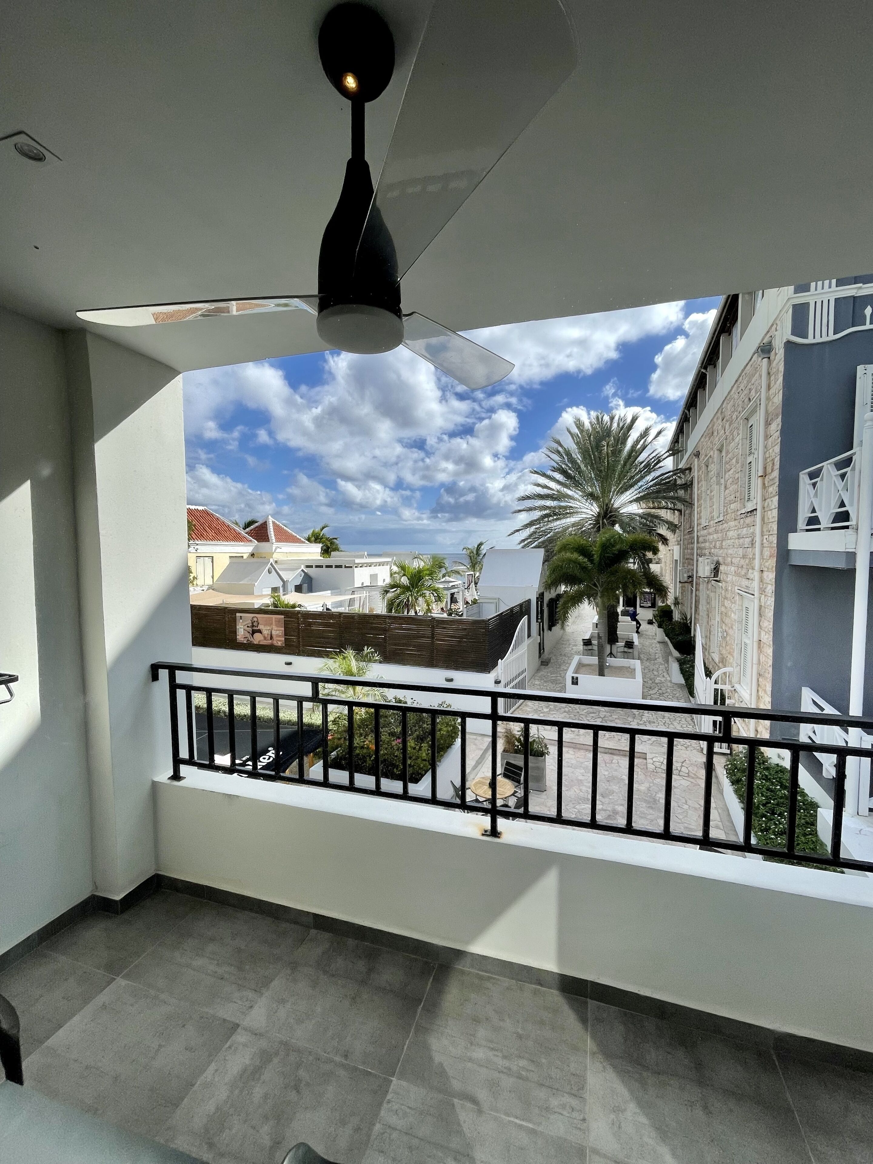 Un balcón con vista a un patio, un ventilador de techo y un cielo despejado.