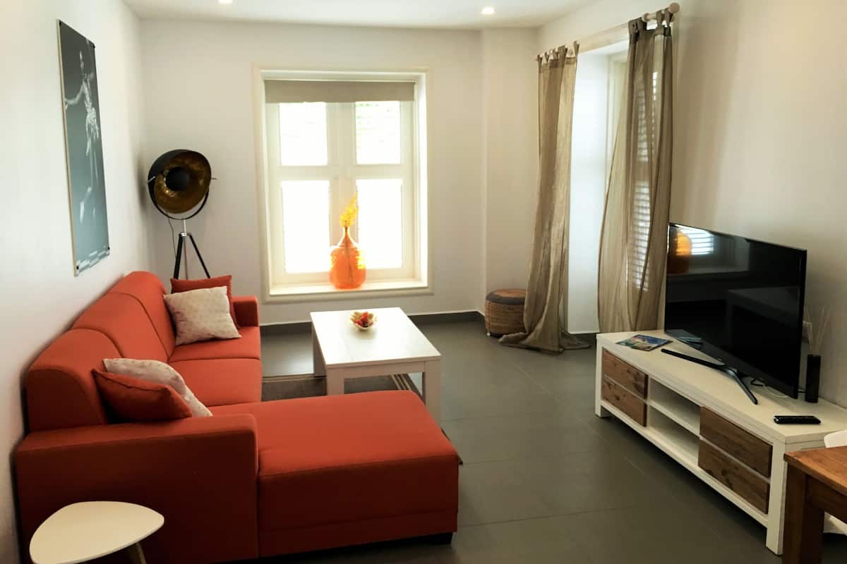 Un salon moderne avec un canapé rouge, une table basse blanche et un téléviseur à écran plat posé sur un meuble en bois.