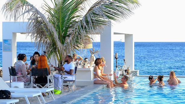 Un espace aménagé au bord de la piscine, avec vue sur la mer, un bar et des coins salon.