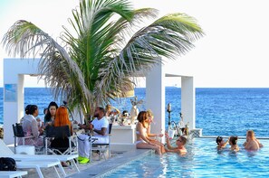 A poolside area with a view of the sea, a bar, and seating arrangements.