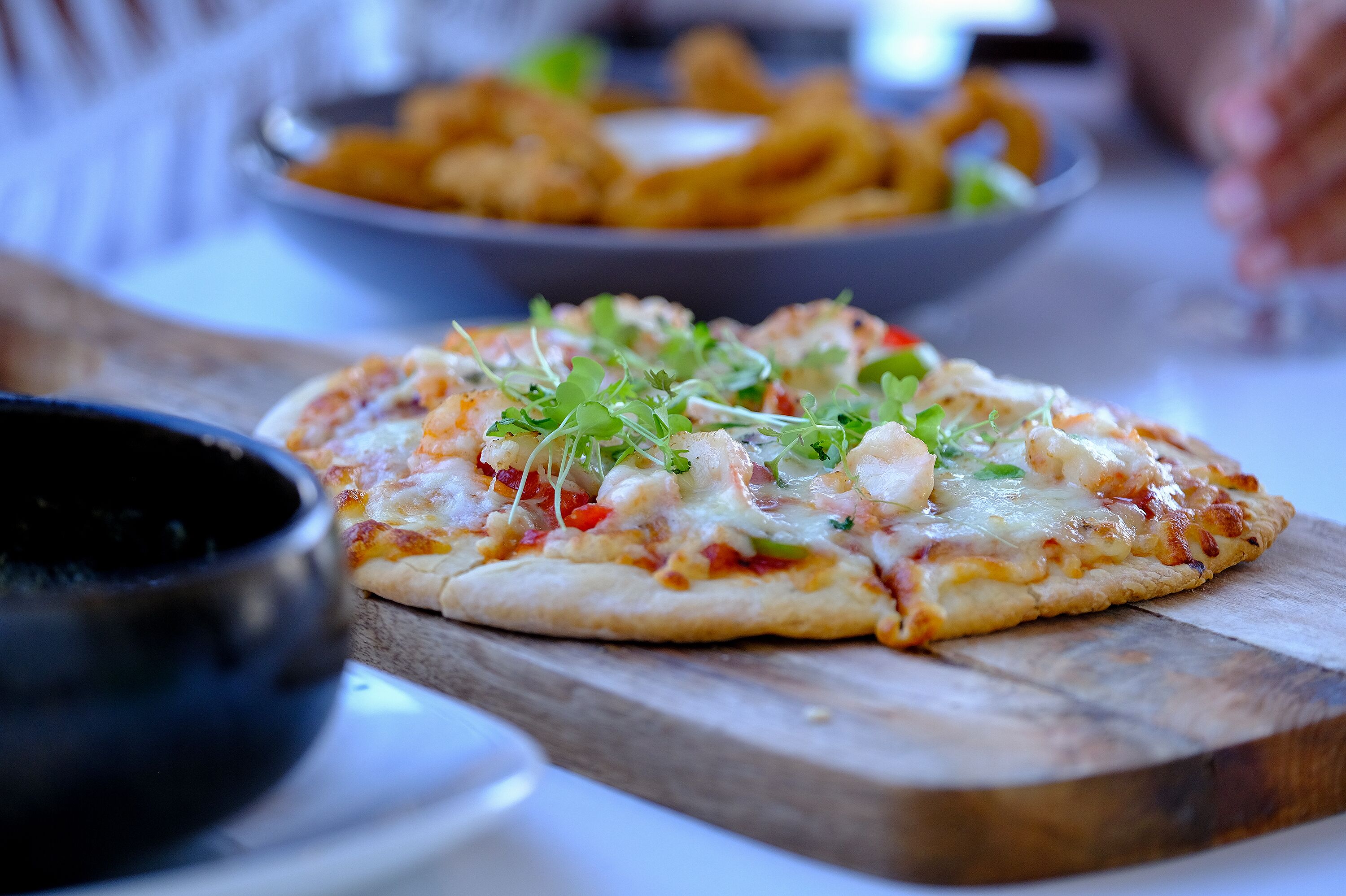 Pizza op een houten plank, met een schaal frietjes op de achtergrond.