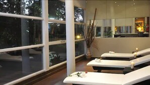 Un cuarto de spa con tres camillas blancas, un ventanal grande y un florero con ramas.