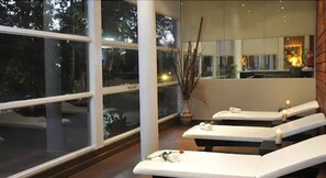 Ein Spa-Raum mit drei weißen Massagetischen, einem großen Fenster und einer Vase mit Zweigen.