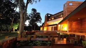 Un edificio moderno de dos pisos con fachada de madera y un área exterior bien iluminada con asientos.