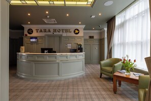 A reception area with a counter, a green chair, a table with a vase of flowers, and a sign that reads 'TARA HOTEL'. - Tara Hotel (Killybegs)