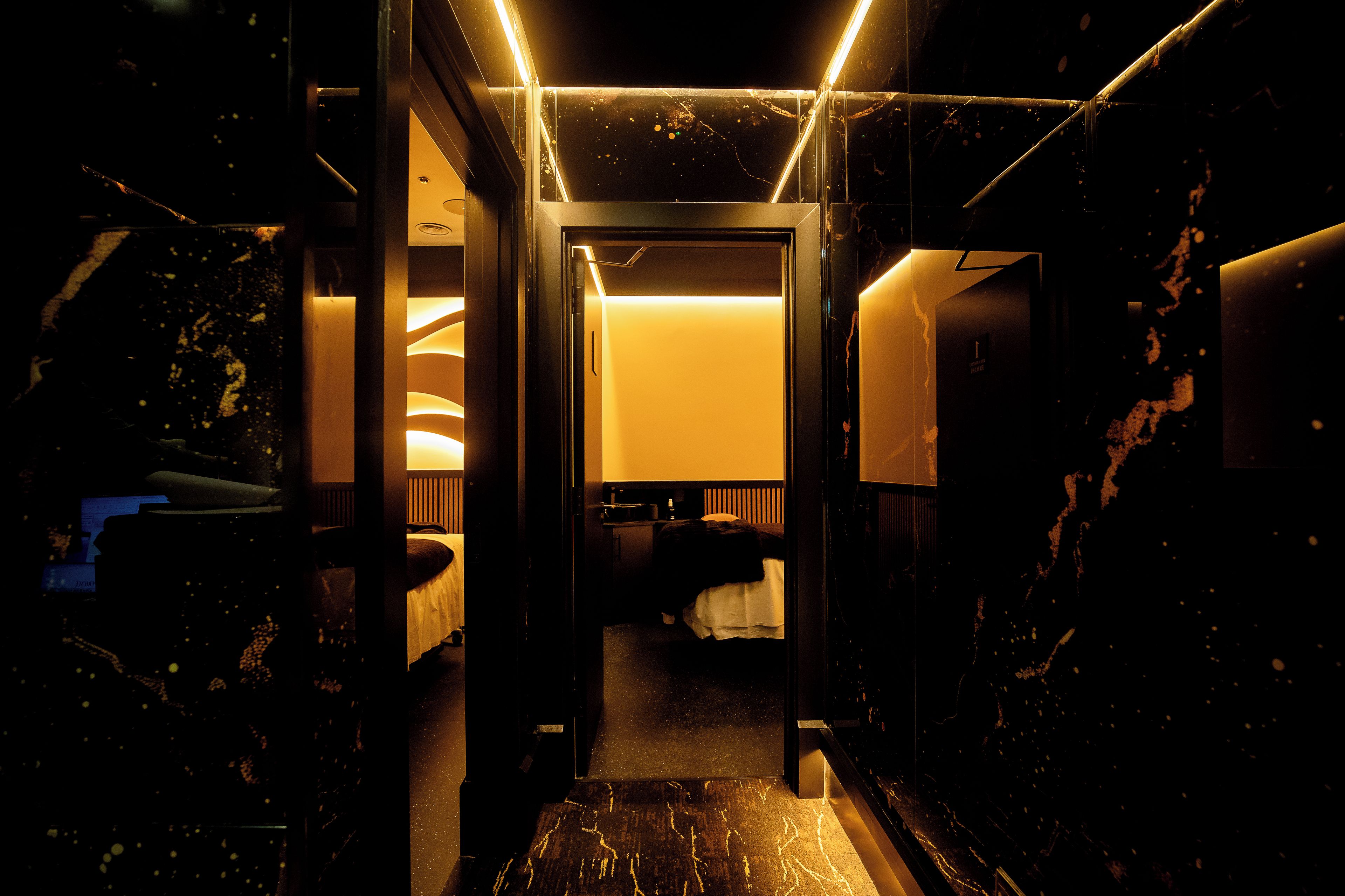 A hotel corridor with a bed, bedside table, and a bathroom visible through an open door.
