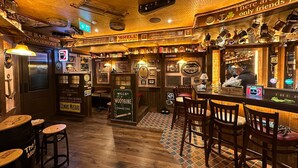 Un bar acogedor con pisos de madera, una barra, taburetes y diversos letreros y recuerdos.