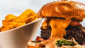 Una hamburguesa con queso y salsa, un cuchillo y un plato de papas fritas.