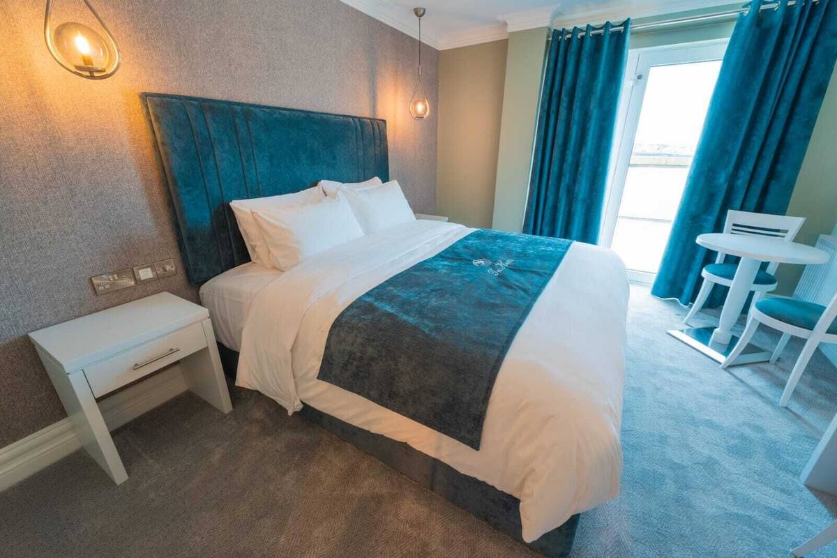 A hotel room with a bed, bedside table, and a small desk with chairs.
