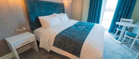 A hotel room with a bed, bedside table, and a small desk with chairs.