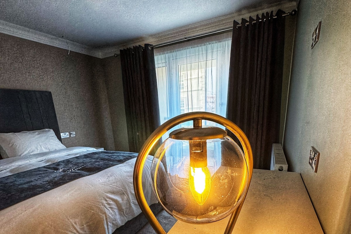 A hotel room with a bed, a bedside table with a lamp, and a window with curtains.